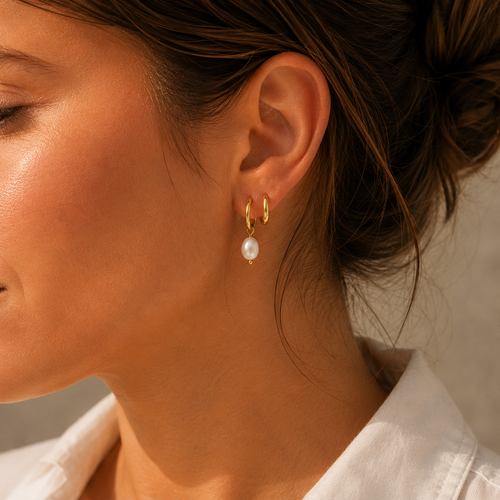 Gold pearl drop hoop earrings worn in sunlight