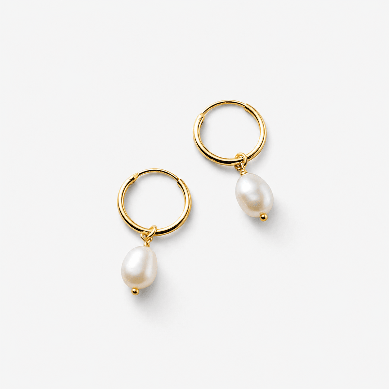 Gold freshwater pearl drop hoop earrings on grey studio background